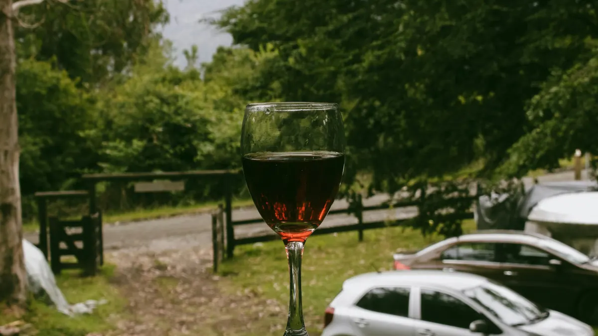 Copa de vino sobre una valla con un coche aparcado al fondo, imagen sobre beber antes de conducir